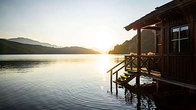 Holzhaus auf Stelzen an einem ruhigen See bei Sonnenuntergang.