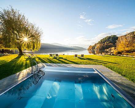 Außenpool mit Liegestühlen auf einer Wiese am See bei Sonnenschein