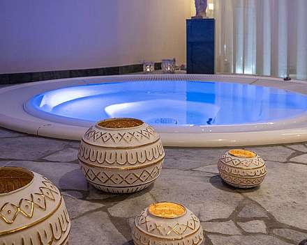 Innenraum mit blau beleuchtetem Whirlpool und dekorativen Keramikgefäßen auf Steinboden.