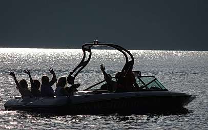 Eine Gruppe winkt in einem Motorboot auf glitzerndem Wasser.