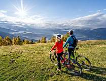 Zwei Mountainbiker stehen auf einer Bergwiese und blicken ins Tal.