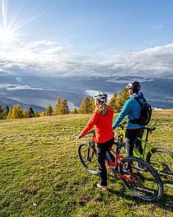 Zwei Mountainbiker stehen auf einer Bergwiese und blicken ins Tal.