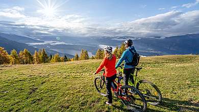 Zwei Mountainbiker stehen auf einer Bergwiese und blicken ins Tal.