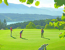 Three golfers on a sunny green with mountain and lake views.