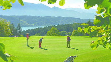 Three golfers on a sunny green with mountain and lake views.