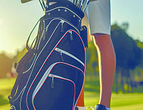 Ein Golfer steht neben einer schwarzen Golfbag mit mehreren Schlägern auf dem Rasen.