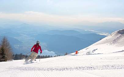 Eine Skifahrerin fährt auf einer verschneiten Piste mit Bergpanorama ab.