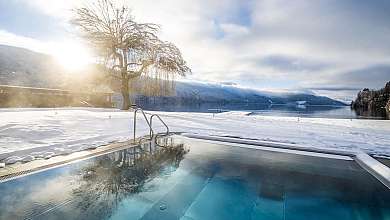 Ein Außenpool im Schnee mit Blick auf einen verschneiten See und Berge.