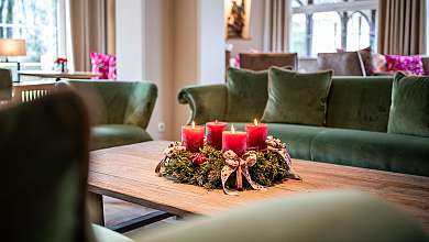 Vier brennende rote Kerzen in einem Adventskranz auf einem Holztisch im Wohnzimmer.