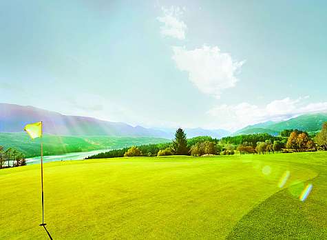 Weite Golfanlage mit Flagge, grünen Fairways, Bergen und sonnigem Himmel.