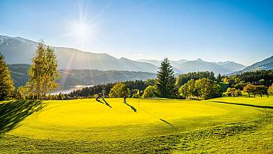 Golfplatzgrün mit zwei Spielern, sonniger Landschaft und Bergen im Hintergrund