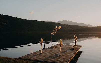 Holzsteg am stillen See mit dekoriertem Bogen und Bergsilhouette im Hintergrund.