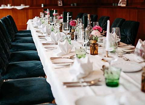 Langer, festlich gedeckter Tisch mit Blumen, Gläsern und dunkelgrünen Stühlen