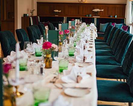 Langer gedeckter Tisch mit Blumen, Gläsern und grünen Samtstühlen im Speisesaal.