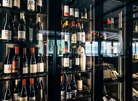 Mehrere Weinflaschen stehen in einem beleuchteten Glaskühlschrank auf Regalen.
