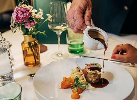 Kellner gießt Sauce über ein angerichtetes Gourmetgericht auf weißem Teller.