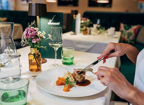 Waiter pours sauce over an arranged gourmet dish on a white plate.