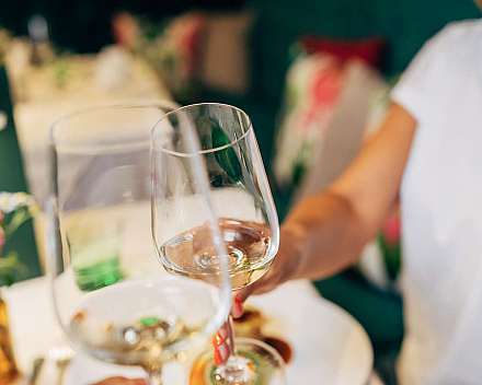 Mehrere Personen stoßen mit Weingläsern an einem Tisch an.