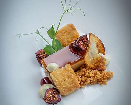 Anrichtetes Dessert mit Feigen, Keksstücken, Creme und grünen Sprossen auf weißem Teller.