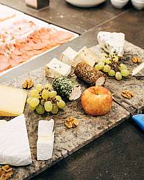 Verschiedene Käsesorten mit Trauben, Nüssen, Apfel und Käsemesser auf einer Steinplatte.