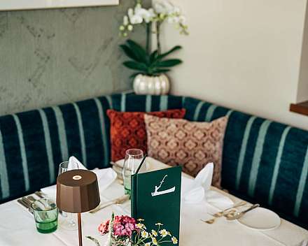 Eingedeckter Restauranttisch mit Blumen, Lampen und gepolsterter Sitzbank