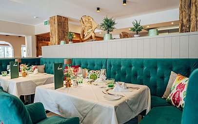 Eleganter Restaurantbereich mit gedeckten Tischen, türkisfarbenen Polstermöbeln und Holzdekoration.