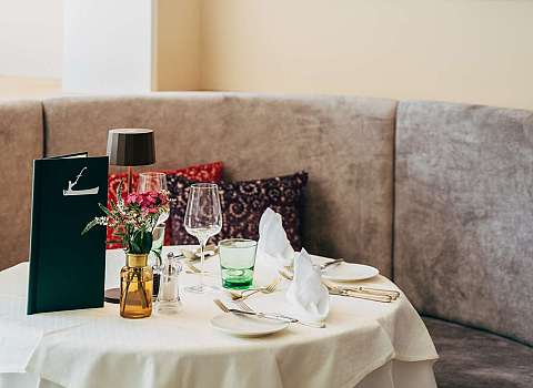 Stilvoll eingerichtetes Restaurant mit gedeckten Tischen, grünen Sitzbänken und hängenden Lampen.