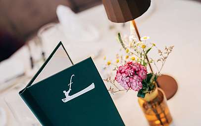 Grüne Karte neben einer kleinen Blumenvasе auf einem hellen Tisch.