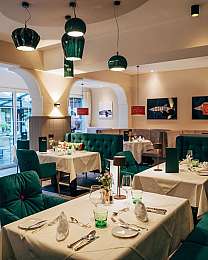 Modernes Restaurant mit gedeckten Tischen, grünen Sitzbänken und hängenden Lampen.