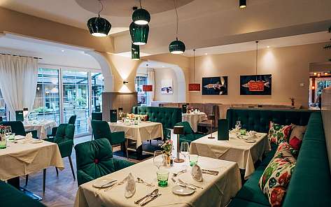 Modernes Restaurant mit grün gepolsterten Sitzbänken, gedeckten Tischen und hängenden Lampen.