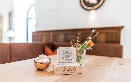 Holztisch mit kleiner Kerze, Blumenvase und Speisekartenhalter in einem hellen Gastraum.