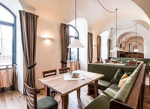 Heller Gastraum mit Holztischen, grünen Sitzbänken und gewölbter Decke.