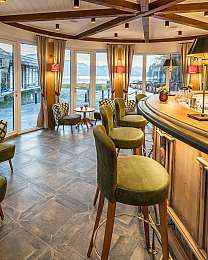 Gemütliche Hotelbar mit grünen Stühlen, Holzdecke und Blick auf den See.