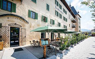 Außenterrasse eines historischen Wirtshauses mit grünen Sonnenschirmen und Fensterläden