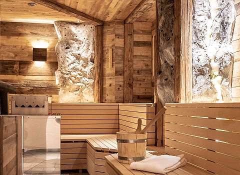 Cosy sauna with wooden panelling, benches and sauna bucket inside.