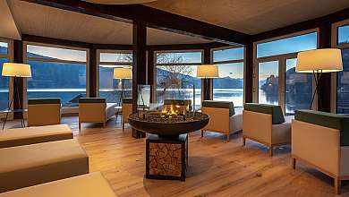 Modernes Lounge-Interieur mit Sesseln, Kamin und großen Fenstern zum See.