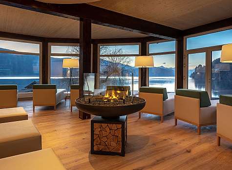Gemütliche Lounge mit Sesseln, Kamin und großen Fenstern zum See
