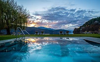Blick auf einen Pool mit Liegestühlen, See und Bergen im Abendlicht.