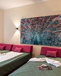 Modernes Zimmer mit drei Betten, Pfauenkunst an der Wand und warmer Beleuchtung.