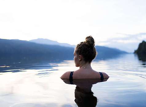 Rückansicht einer Frau im ruhigen See vor Bergen bei hellem Himmel.