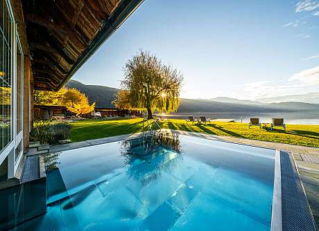 Outdoor pool with sun loungers, lawn and views of a calm lake at sunrise