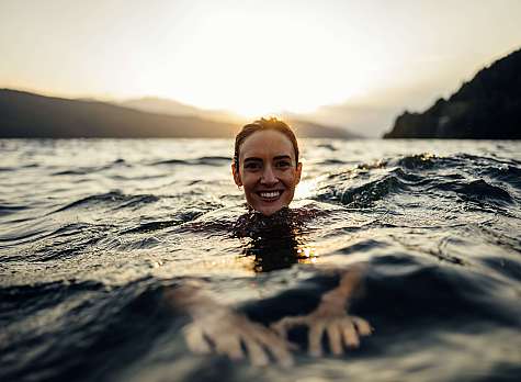 Frau schwimmt im offenen Wasser vor Bergen bei Sonnenuntergang.
