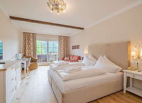 Helles Hotelzimmer mit Doppelbett, Sitzecke und Balkonblick auf die Berge.