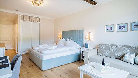Helles Schlafzimmer mit Doppelbett, Sofa, Couchtisch und Holzbalken an der Decke.