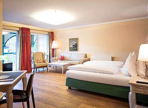 Helles Schlafzimmer mit Doppelbett, Sofa, Sessel, Beistelltisch und großen Fenstern.
