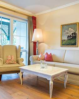 Helles Wohnzimmer mit Sofa, Sessel, Couchtisch, Stehlampe und großen Fenstern.