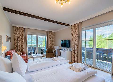 Gemütliches Hotelzimmer mit Doppelbett, Balkon und Blick auf Berge und See.