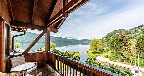 Wooden balcony with wicker chairs and a view of a calm lake and green hills