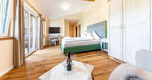 Helles Schlafzimmer mit Holzboden, Doppelbett, Schrank und Balkonfenstern.