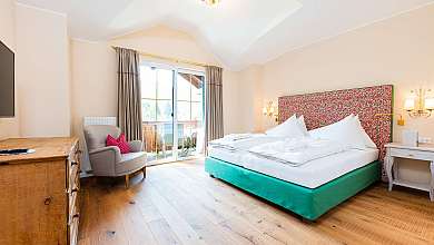 Bright bedroom with large bed, armchair, wooden dresser and balcony window.
